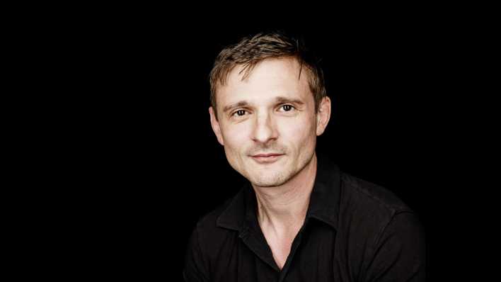 Porträt des Schauspielers Florian Lukas, mit schwarzem Hemd vor dunklem Hintergrund (Quelle: Jan Rickers) Porträt des Schauspielers Florian Lukas, mit schwarzem Hemd vor dunklem Hintergrund (Quelle: Jan Rickers)